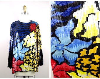 May include: A long-sleeved sequined top featuring a colourful floral pattern in shades of red, yellow, blue, and black. The sequins are arranged in a mosaic-like design, creating a textured and eye-catching effect.