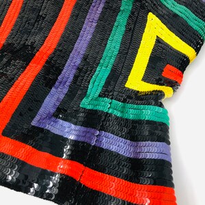 May include: A black fabric with colourful stripes of red, purple, green, and yellow sequins. The sequins are arranged in a geometric pattern.
