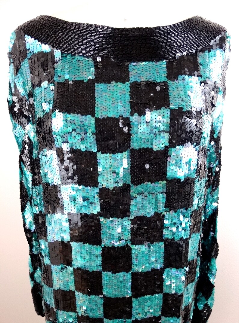 Puede incluir: Una blusa de lentejuelas negra y turquesa con un patr&oacute;n de cuadros. La blusa tiene un escote redondo y est&aacute; hecha de una tela suave y el&aacute;stica.