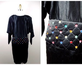 May include: A black satin dress with long sleeves and a jeweled belt. The belt is made of a quilted fabric with colorful rhinestones.