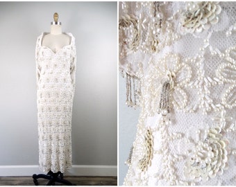 May include: A white beaded and sequined maxi dress with a sweetheart neckline and long sleeves. The dress is adorned with pearl-like beads and sequins, creating a luxurious and elegant look.