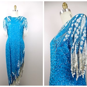 May include: A turquoise sequined dress with white beaded fringe. The dress has a fitted bodice and a flowing skirt. The sleeves are short and have a beaded fringe detail.
