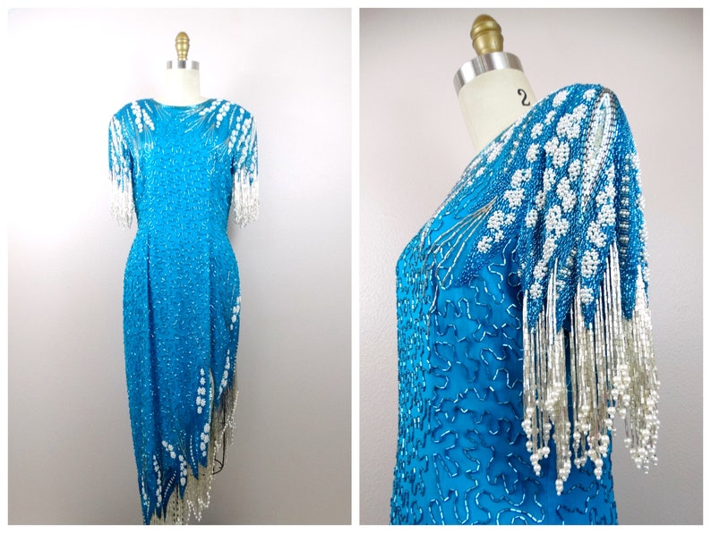 May include: A turquoise sequined dress with white beaded fringe. The dress has a fitted bodice and a flowing skirt. The sleeves are short and have a beaded fringe detail.