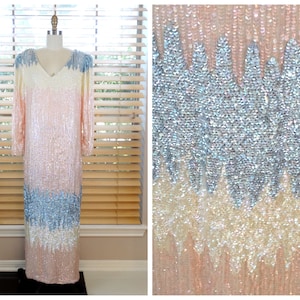 May include: A long, sequined dress in shades of pink, white, and blue. The dress has a V-neckline and long sleeves. The sequins are arranged in a pattern that creates a gradient effect.