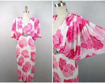 May include: A white and pink floral print dress with a sequined bodice and a large jeweled belt. The dress has a V-neckline and short, puffed sleeves.