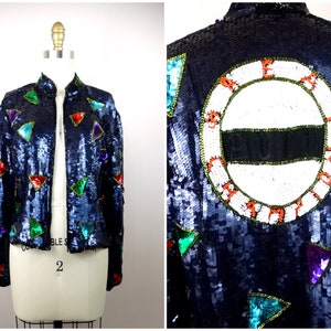 May include: A navy blue sequined jacket with a white circle on the back that says "COUNT YOUR BLESSINGS". The jacket is decorated with colorful triangle sequins.