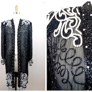 Könnte beinhalten: Eine schwarze und weiße Perlen-Cardigan mit einem langen, offenen Vorderteil. Die Cardigan ist aus durchsichtigem Stoff und hat ein zartes Blumenmuster.