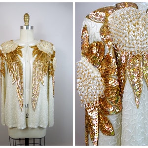 May include: Ivory-colored sequined jacket with gold and white beaded embellishments. The jacket features a round neckline and long sleeves. Gold sequin and beaded floral designs adorn the shoulders and front, creating a glamorous look. The jacket is displayed on a mannequin.