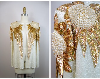 Könnte beinhalten: Elfenbeinfarbene Paillettenjacke mit gold- und weißfarbenen Perlenverzierungen. Die Jacke hat einen runden Ausschnitt und lange Ärmel. Goldene Pailletten- und Perlenblumendesigns zieren die Schultern und die Vorderseite und sorgen für einen glamourösen Look. Die Jacke wird auf einer Schaufeniquin präsentiert.