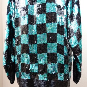 Puede incluir: Una blusa de lentejuelas azul verdoso y negro con un patr&oacute;n de cuadros. La blusa tiene mangas largas y un corte holgado.