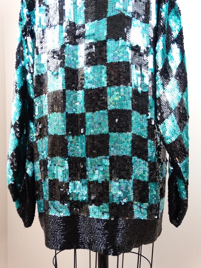 Puede incluir: Una blusa de lentejuelas azul verdoso y negro con un patr&oacute;n de cuadros. La blusa tiene mangas largas y un corte holgado.