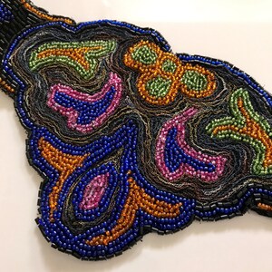 Peut inclure: Gros plan sur une embellissement en perles avec un motif en spirale dans des tons de bleu, vert, orange et rose. Les perles sont cousues sur une base en tissu noir.