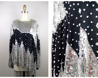 May include: A black and silver sequined top with a geometric design. The top has long sleeves and a loose fit.
