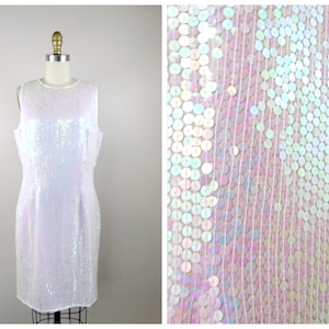 May include: A white sleeveless dress made of iridescent sequins. The sequins are arranged in a vertical pattern, creating a shimmering effect.