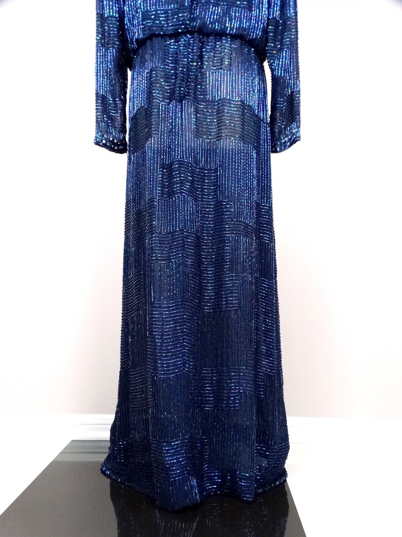 May include: A long, navy blue sequined dress with a geometric pattern. The dress has long sleeves and a fitted bodice.