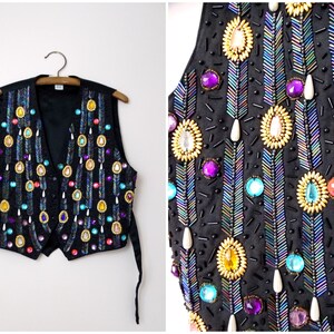 Op de afbeelding: Een zwart vest met een parelmoer ontwerp. Het vest is versierd met iriserende pailletten, gekleurde kralen en gouden accenten. Het vest heeft een V-hals en twee lange banden.