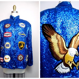 Könnte beinhalten: Eine blaue Paillettenjacke mit verschiedenen gestickten Aufnähern, darunter Autologos und ein großer Adler auf der Rückseite.