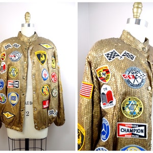 May include: A gold sequined bomber jacket with a variety of embroidered car and racing patches. The patches include logos for Porsche, Ferrari, Corvette, and Champion Spark Plugs.