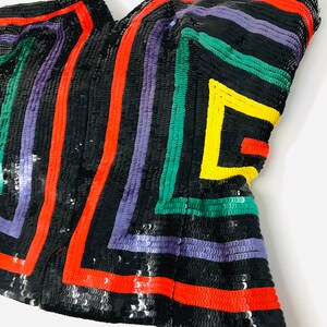May include: A black sequined strapless top with a geometric pattern in red, yellow, green, and purple.