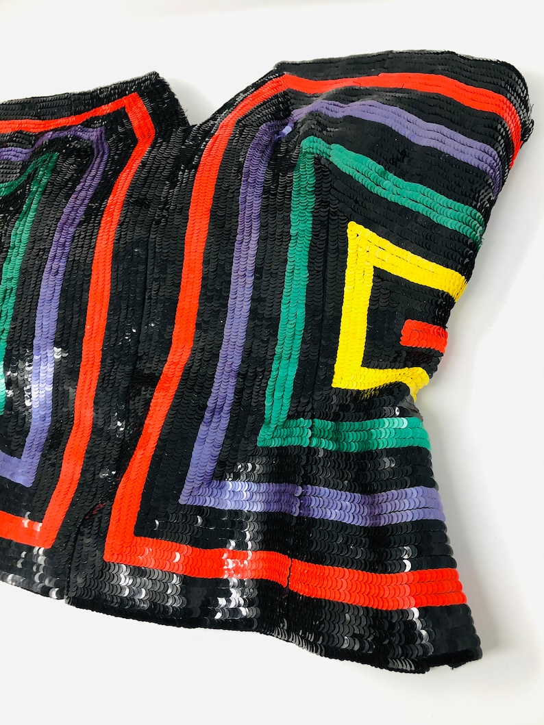 May include: A black sequined strapless top with a geometric pattern in red, yellow, green, and purple.