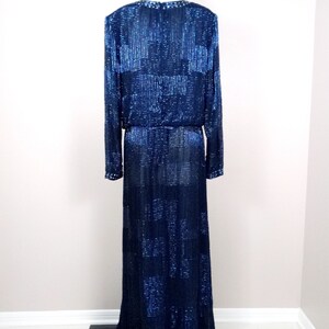 May include: A long, navy blue sequined gown with a long sleeve design. The gown has a fitted bodice and a flowing skirt.