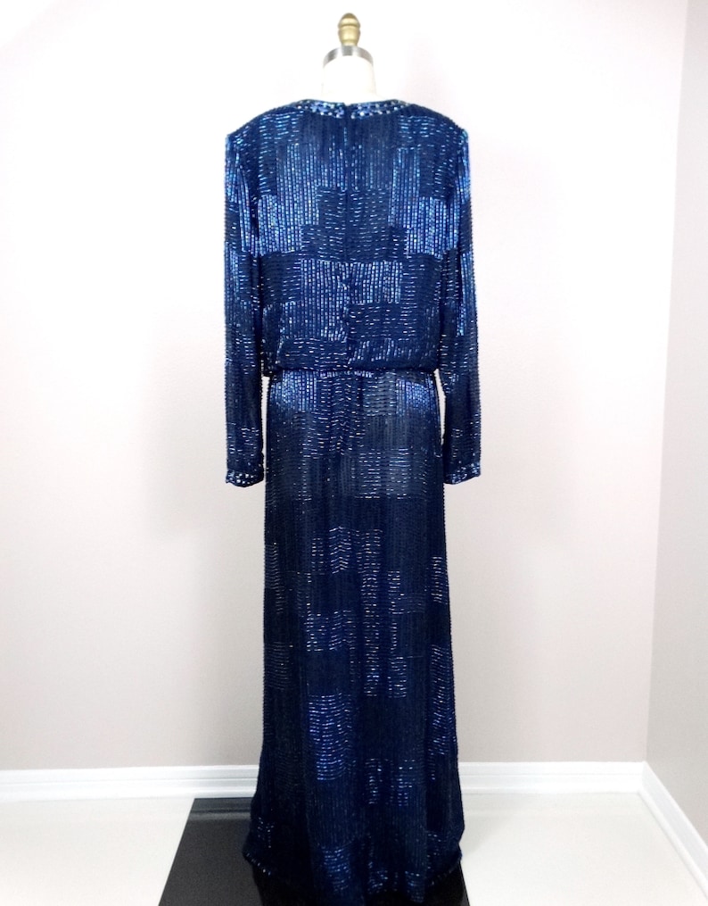 May include: A long, navy blue sequined gown with a long sleeve design. The gown has a fitted bodice and a flowing skirt.