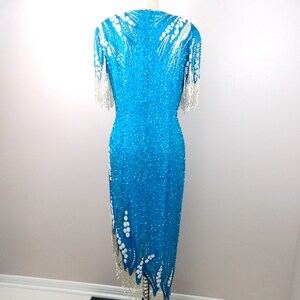 May include: A turquoise sequined dress with white beaded embellishments and fringe. The dress has a fitted bodice and a flowing skirt.