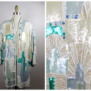 May include: A long, open-front, sequined jacket with a geometric pattern in shades of white, silver, green, and blue. The jacket is made of a lightweight fabric and has a relaxed fit.