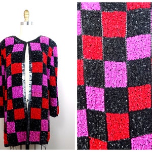 Puede incluir: Una chaqueta de lentejuelas negra, roja y rosa con un patrón de cuadros. La chaqueta está abierta en la parte delantera y tiene mangas largas.