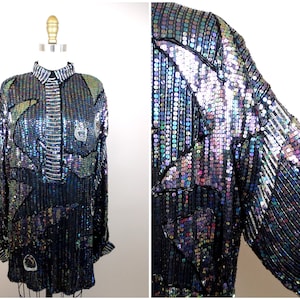 Könnte beinhalten: Ein langärmliges, irisierendes Paillettenhemd mit geometrischem Muster in Schwarz und Silber. Das Hemd hat einen Knopfleisten vorne und einen Kragen.