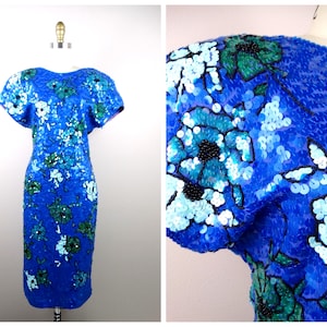 May include: A blue sequined dress with a floral pattern in shades of blue, green, and black. The dress has short sleeves and is displayed on a mannequin. The sequins create a shimmering effect.