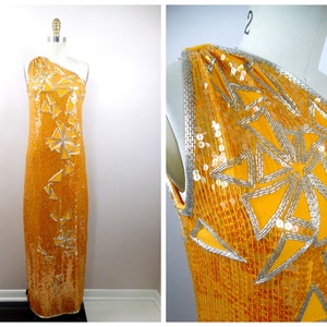 K&ouml;nnte beinhalten: Ein langes, einarmige Kleid in leuchtend gelber Farbe mit silbernen Pailletten und geometrischen Mustern. Das Kleid ist aus einem weichen, flie&szlig;enden Stoff gefertigt und hat eine schmeichelhafte Silhouette.
