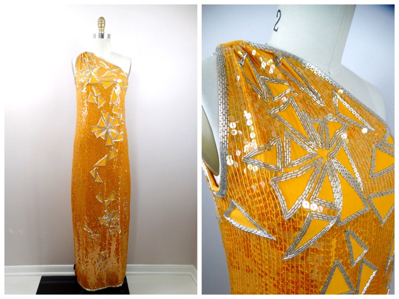 K&ouml;nnte beinhalten: Ein langes, einarmige Kleid in leuchtend gelber Farbe mit silbernen Pailletten und geometrischen Mustern. Das Kleid ist aus einem weichen, flie&szlig;enden Stoff gefertigt und hat eine schmeichelhafte Silhouette.