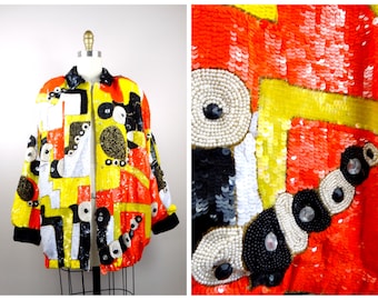 Può includere: Una giacca colorata con paillettes con un motivo geometrico in tonalità di rosso, giallo, nero e bianco. La giacca ha una chiusura a zip e un colletto.