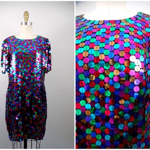 Puede incluir: Un vestido de manga corta hecho de lentejuelas iridiscentes en una variedad de colores, incluyendo rosa, azul, verde y dorado. Las lentejuelas están dispuestas en un patrón circular.