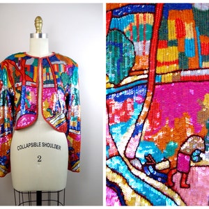 Può includere: Una giacca di paillettes colorata con un motivo geometrico. La giacca è corta e senza colletto. Il testo "COLLAPSIBLE SHOULDER 2" è stampato sulla giacca.