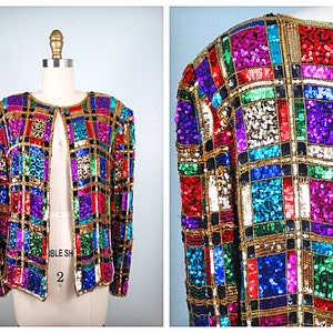 Puede incluir: Una chaqueta de lentejuelas de colores con un patrón geométrico en tonos de rojo, azul, verde, dorado y morado. La chaqueta tiene un cierre frontal y mangas largas.