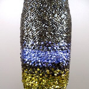 May include: A short, sleeveless dress made of sequins. The dress is black with a band of purple sequins at the bottom and a band of gold sequins at the hem.