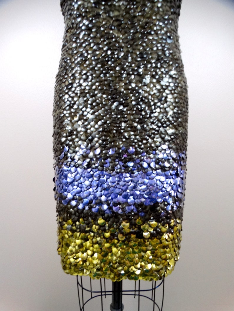 May include: A short, sleeveless dress made of sequins. The dress is black with a band of purple sequins at the bottom and a band of gold sequins at the hem.