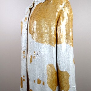 May include: A white and gold sequined button-up shirt with a long sleeve. The shirt has a geometric pattern with large white and gold shapes.