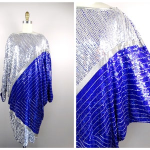 May include: A sequined tunic dress in silver and royal blue, displayed on a mannequin. The dress features a diagonal color block design with silver sequins on the top and royal blue sequins on the bottom. The sleeves are long and the neckline is wide.