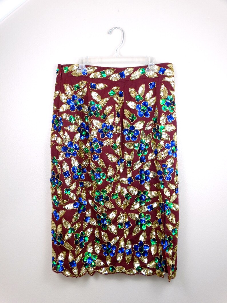 Puede incluir: Una falda color burdeos con un estampado floral hecho de lentejuelas doradas, azules y verdes.