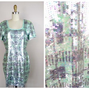 May include: A short-sleeved, mint green and silver sequined dress with a square neckline. The dress has a geometric pattern and is made of iridescent sequins.