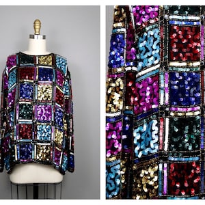 Puede incluir: Una blusa de lentejuelas de manga larga con un patrón geométrico en tonos de azul, rojo, dorado y morado.
