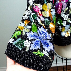 Pode incluir: Uma jaqueta preta de contas com um design floral. A jaqueta &eacute; coberta de lantejoulas e contas em v&aacute;rias cores, incluindo azul, verde, rosa e amarelo.