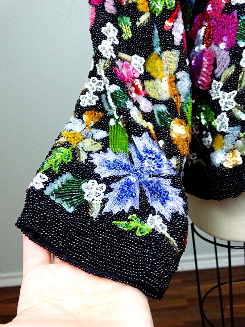 Pode incluir: Uma jaqueta preta de contas com um design floral. A jaqueta &eacute; coberta de lantejoulas e contas em v&aacute;rias cores, incluindo azul, verde, rosa e amarelo.