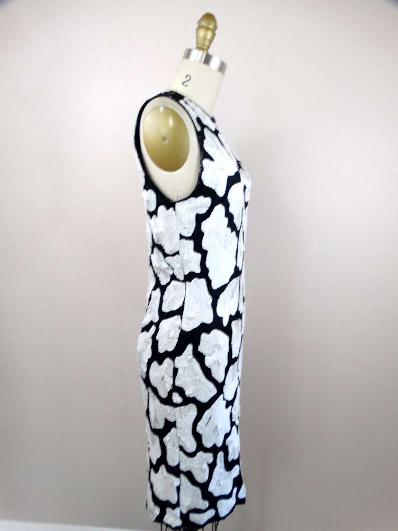 May include: A sleeveless black and white dress with a unique, abstract pattern. The dress is made of a textured fabric and has a fitted silhouette.