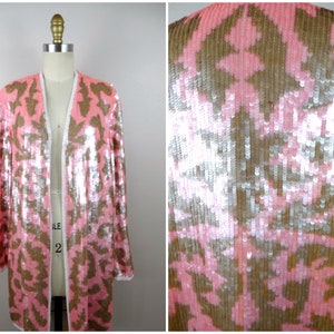 May include: A pink sequined jacket with a white trim and a brown patterned design. The jacket is displayed on a mannequin. The sequins create a shimmering effect, adding a touch of glamour to the garment. The jacket is a statement piece.