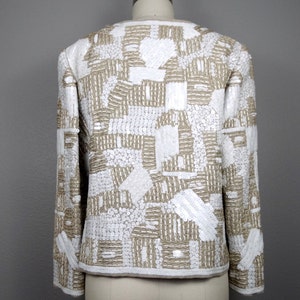 May include: A white and gold sequined jacket with a geometric pattern. The jacket has long sleeves and a cropped length.