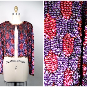 Peut inclure: Une veste en sequins violette et rose avec une coupe courte et une ouverture sur le devant. La veste porte une étiquette 'Collapsible Shoulder 2' sur le devant.
